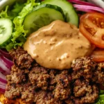 Close-up of a delicious Beef Burger Bowl Recipe featuring seasoned ground beef, fresh lettuce, sliced cucumbers, tomatoes, red onions, and a creamy special sauce.